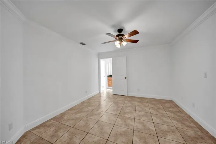 Spare room featuring a ceiling fan, crown molding, and light tile patterned floors