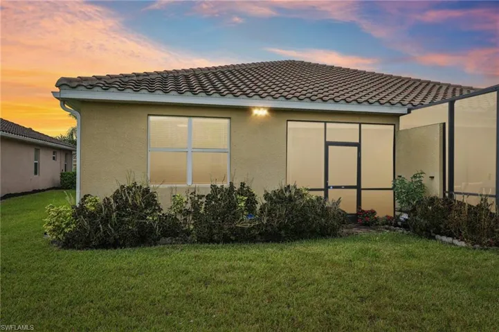 Back of house at dusk with a lawn, stucco siding, and a tiled roof