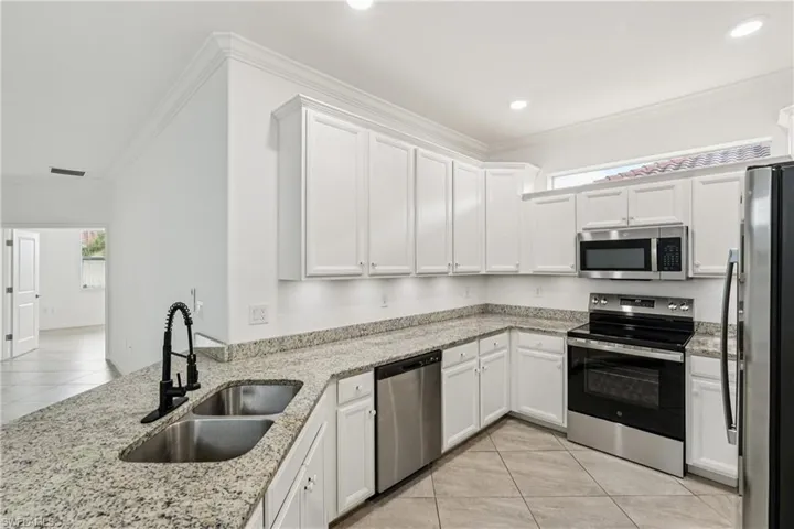 Kitchen featuring stainless steel appliances, light tile patterned flooring, white cabinetry, crown molding, and light stone countertops