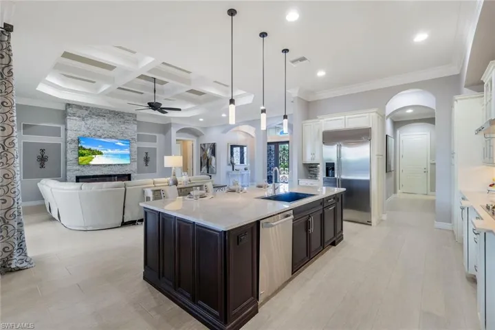Kitchen featuring coffered ceiling, a stone fireplace, a center island with sink, white cabinets, and appliances with stainless steel finishes