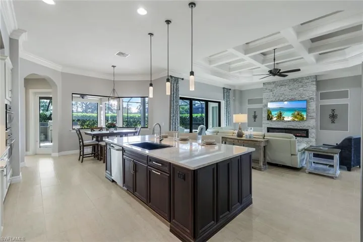Kitchen featuring light stone countertops, sink, white cabinetry, hanging light fixtures, and a stone fireplace