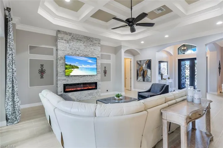 Living room featuring a stone fireplace, crown molding, beamed ceiling, and coffered ceiling