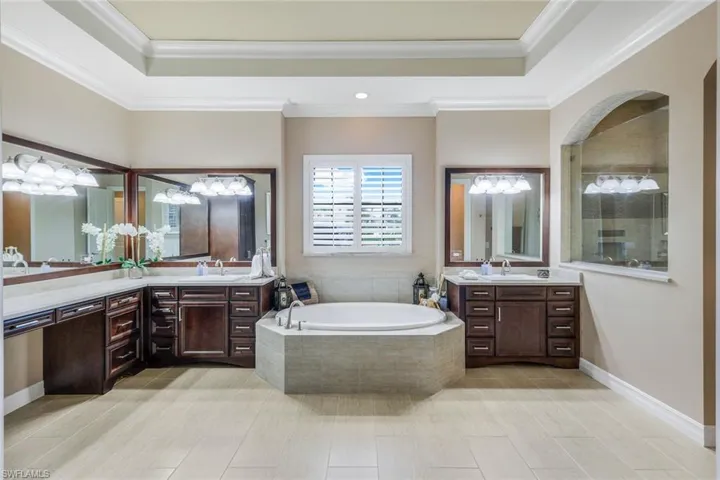 This spacious bathroom exudes elegance with its light beige and tan color palette, enhanced by wood-plank-style tile floors and dark-stained wood cabinetry.