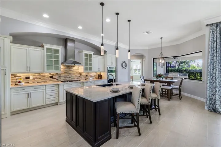 Kitchen featuring pendant lighting, a kitchen island with sink, white cabinets, wall chimney exhaust hood, and light stone counters