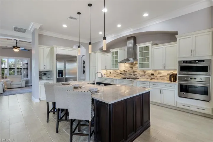 Kitchen featuring wall chimney exhaust hood, stainless steel appliances, a kitchen island with sink, sink, and pendant lighting
