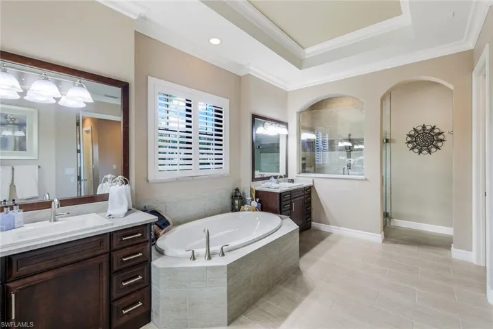 A rounded soaking tub is nestled between dual vanities with modern sinks and light countertops, while a large dark-framed mirror reflects the room's refined details.