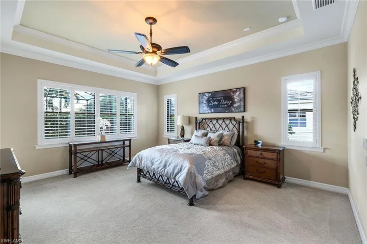 Carpeted bedroom with a tray ceiling, ceiling fan, and ornamental molding