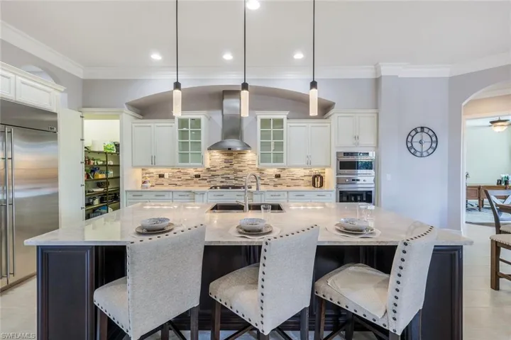 Kitchen featuring appliances with stainless steel finishes, wall chimney exhaust hood, and an island with sink