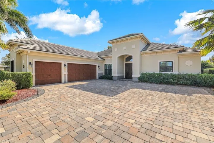 The medium-brown double and single garage doors complement the light brownish-beige paver stone driveway, bordered by neatly trimmed hedges.