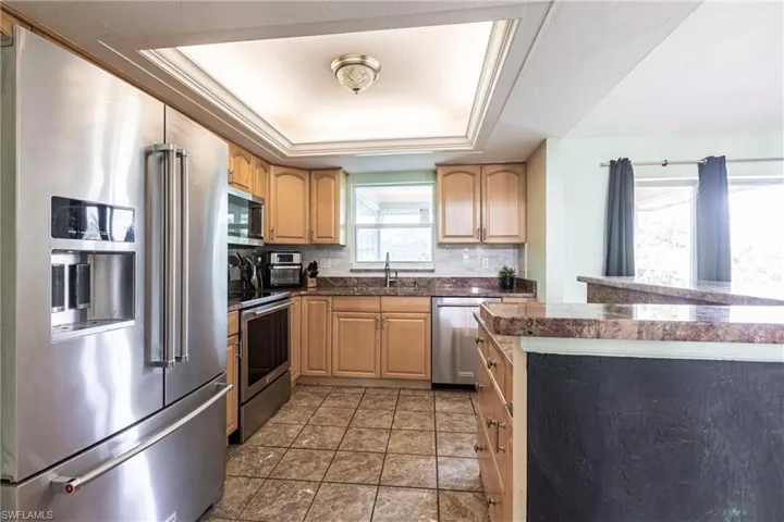 Kitchen featuring stainless steel appliances, a raised ceiling, a sink, backsplash, and light brown cabinetry