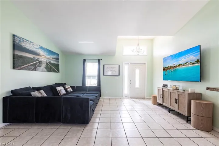 Living area featuring a chandelier, light tile patterned floors, baseboards, and lofted ceiling