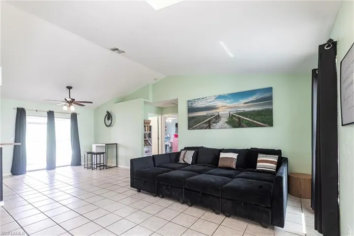 Living room with lofted ceiling, light tile patterned flooring, and a ceiling fan