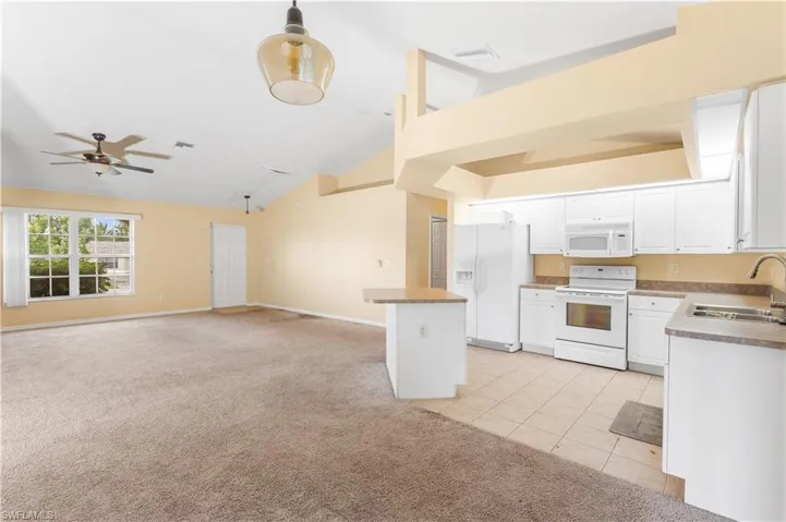 Kitchen featuring open floor plan, light carpet, white appliances, white cabinets, and light tile patterned flooring