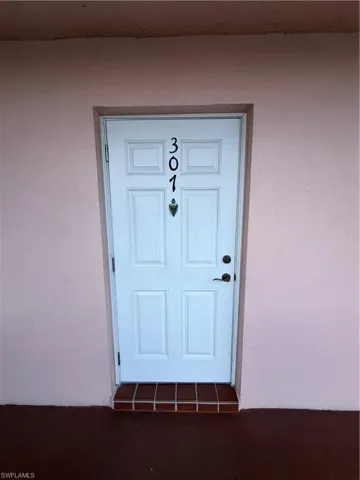 White paneled entry door featuring dark hardware and a decorative knocker