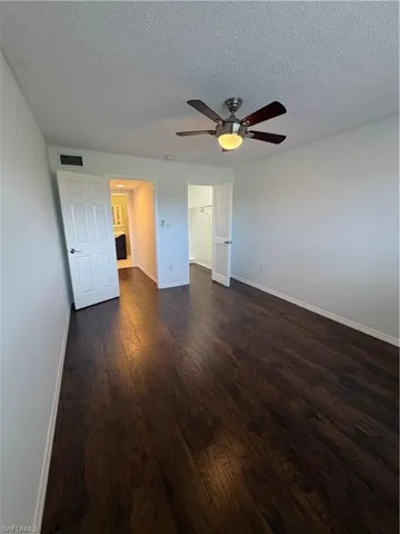 Spacious room featuring dark wood-finish flooring, a ceiling fan with integrated lighting, and white paneled doors