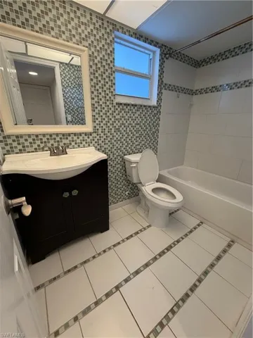 Bathroom featuring a dark wood-finish vanity with an integrated sink, mosaic tile accent walls, a bathtub with white subway tile surround, and white floor tiles with mosaic inlay strips