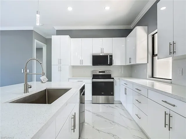 Kitchen featuring stainless steel appliances, light stone counters, ornamental molding, white cabinetry, and hanging light fixtures