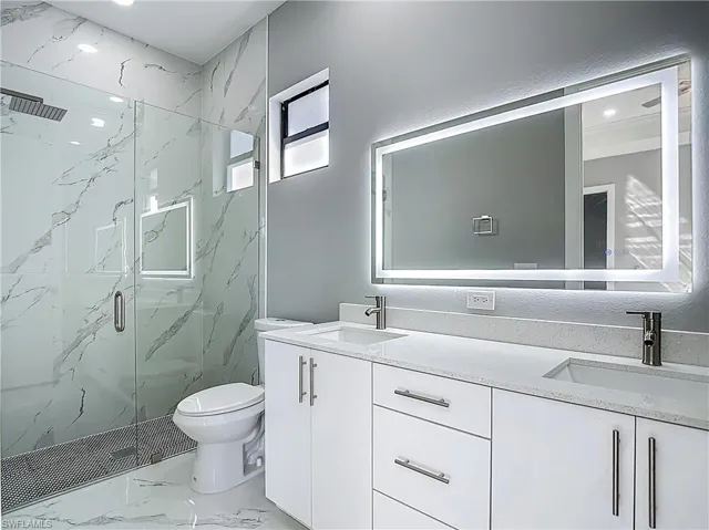 Full bath featuring double vanity, a marble finish shower, light marble finish flooring, and recessed lighting