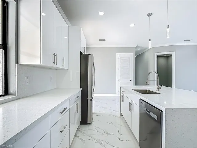 Kitchen with light stone countertops, white cabinets, stainless steel appliances, and ornamental molding