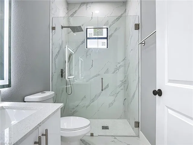 Full bath featuring vanity, a marble finish shower, and a textured wall