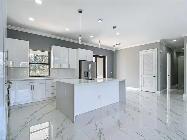 Kitchen with an island with sink, stainless steel refrigerator with ice dispenser, crown molding, pendant lighting, and light stone counters