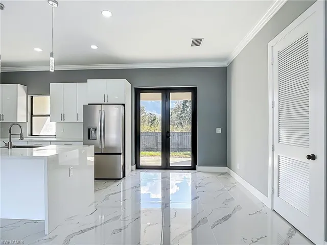 Kitchen with french doors, stainless steel fridge with ice dispenser, light marble finish floors, crown molding, and light stone counters