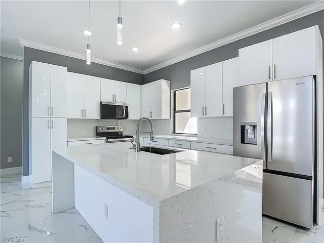 Kitchen featuring stainless steel appliances, pendant lighting, white cabinets, crown molding, and light stone counters