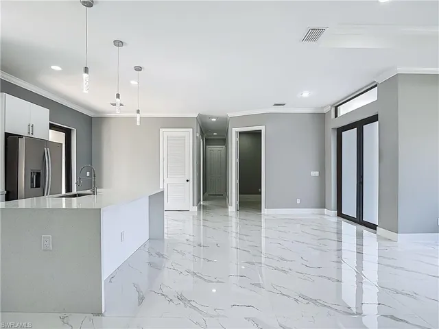 Kitchen featuring white cabinetry, stainless steel fridge, light stone countertops, crown molding, and a kitchen island with sink