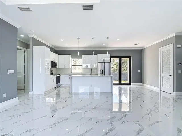 Kitchen featuring pendant lighting, a center island with sink, light countertops, white cabinetry, and stainless steel appliances