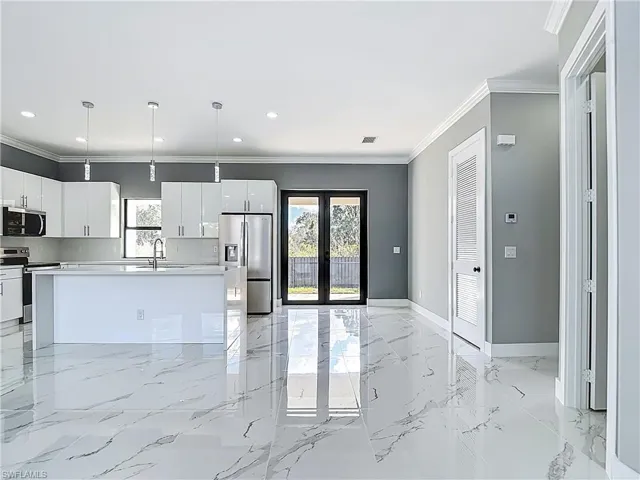 Kitchen featuring french doors, stainless steel appliances, decorative light fixtures, ornamental molding, and white cabinetry