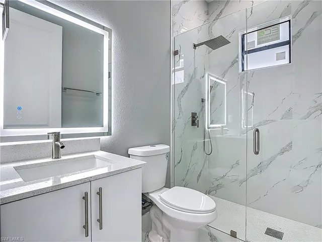 Full bath with a marble finish shower, vanity, and a textured wall