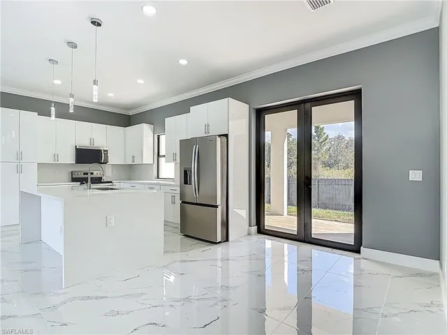 Kitchen featuring stainless steel appliances, hanging light fixtures, white cabinets, ornamental molding, and light stone counters