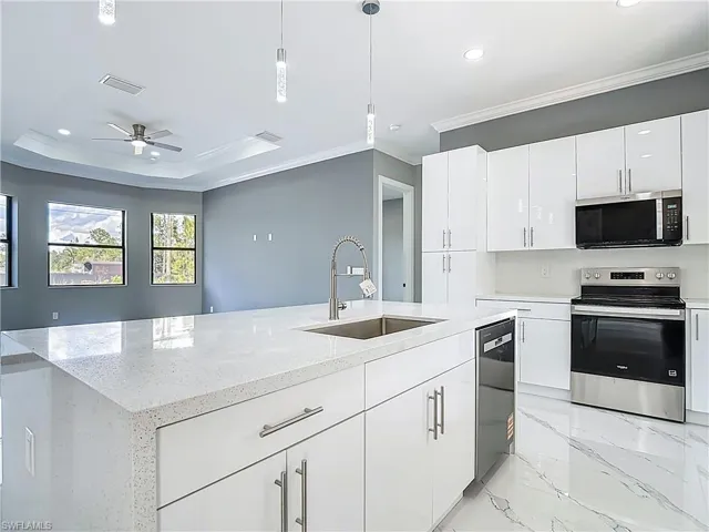 Kitchen featuring stainless steel appliances, white cabinetry, light stone countertops, ceiling fan, and ornamental molding