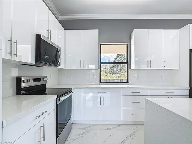 Kitchen featuring stainless steel appliances, light marble finish floors, ornamental molding, white cabinets, and light stone countertops