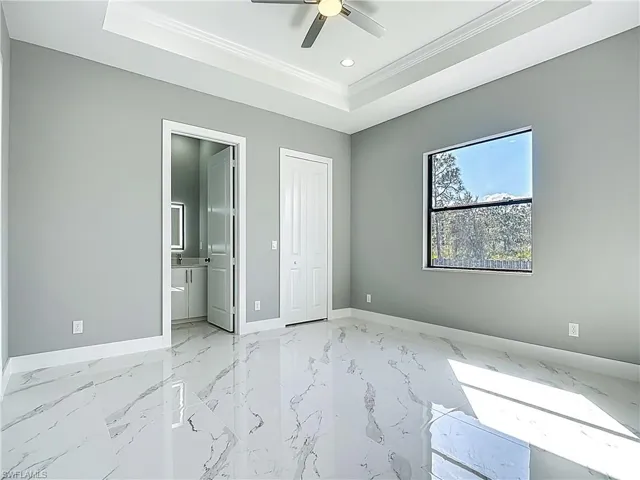 Unfurnished bedroom with a tray ceiling, crown molding, recessed lighting, a ceiling fan, and light marble finish flooring