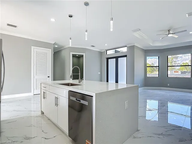 Kitchen featuring crown molding, light stone counters, stainless steel dishwasher, a kitchen island with sink, and white cabinetry