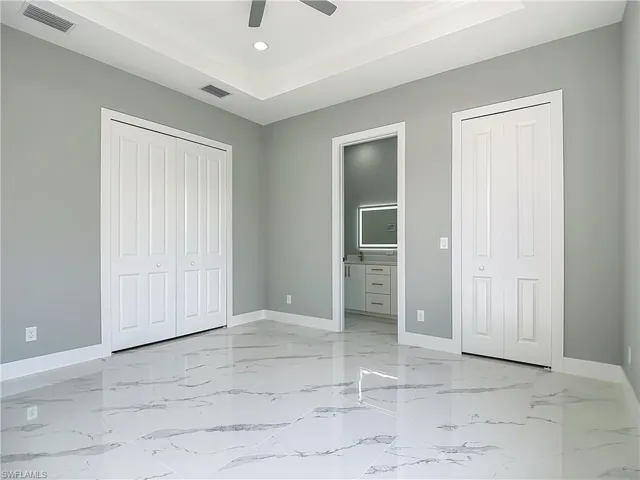 Unfurnished bedroom featuring a raised ceiling, connected bathroom, a ceiling fan, two closets, and recessed lighting