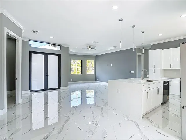 Kitchen featuring french doors, ceiling fan, a kitchen island with sink, ornamental molding, and white cabinets