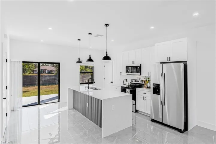 Kitchen with stainless steel appliances, light marble finish flooring, decorative light fixtures, light stone countertops, and white cabinetry