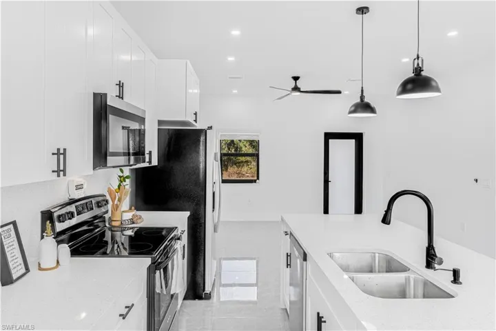 Kitchen with stainless steel appliances, white cabinetry, light stone countertops, decorative light fixtures, and recessed lighting