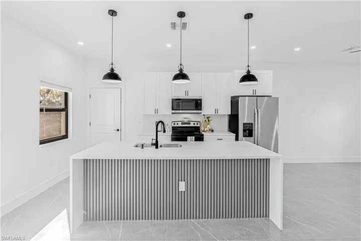 Kitchen with light stone countertops, appliances with stainless steel finishes, a kitchen island with sink, pendant lighting, and white cabinetry