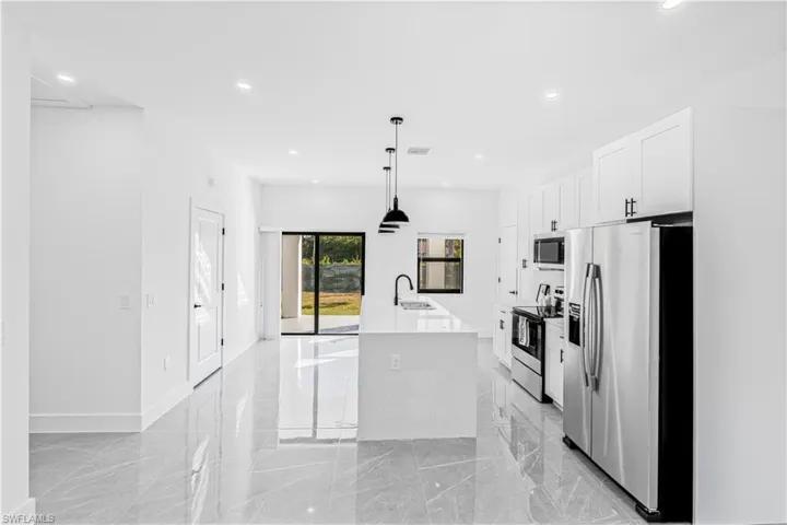 Kitchen with stainless steel appliances, pendant lighting, light stone countertops, an island with sink, and light marble finish floors