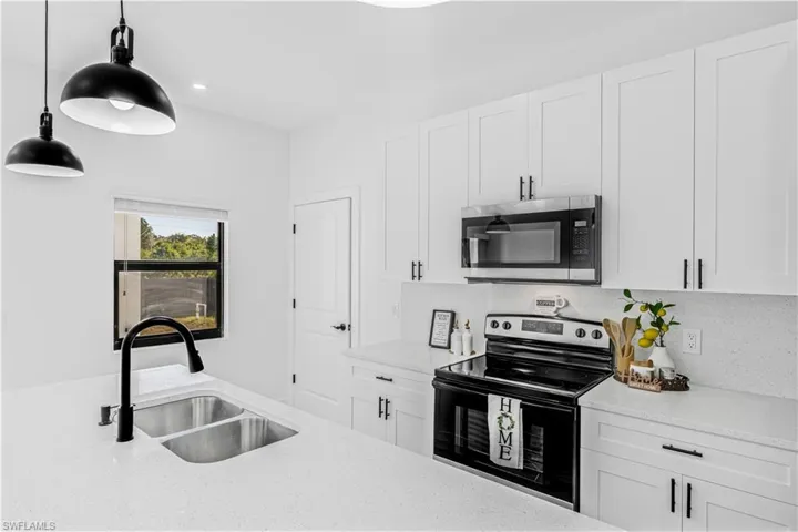 Kitchen with appliances with stainless steel finishes, white cabinetry, light stone countertops, hanging light fixtures, and recessed lighting