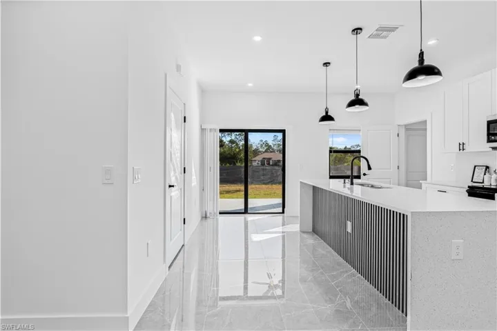 Kitchen with light marble finish flooring, light stone countertops, hanging light fixtures, white cabinetry, and recessed lighting
