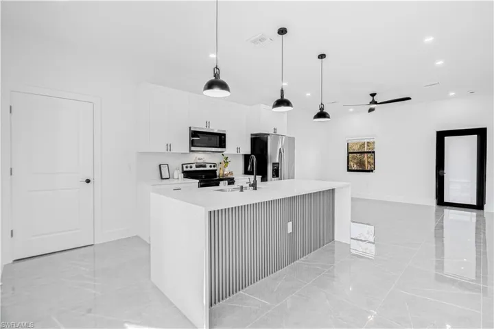 Kitchen featuring a ceiling fan, pendant lighting, appliances with stainless steel finishes, light stone countertops, and light marble finish floors