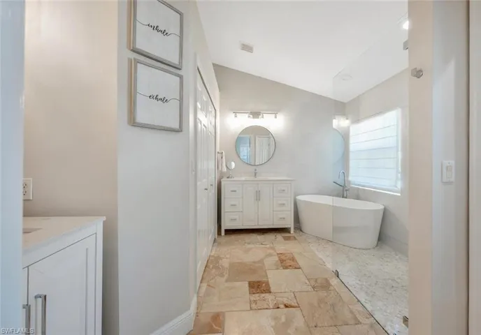 Bathroom with a bathtub, tile patterned flooring, tile walls, vanity, and vaulted ceiling