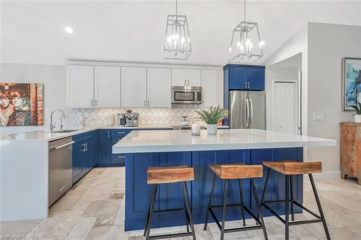 Kitchen featuring appliances with stainless steel finishes, light tile patterned flooring, blue cabinets, backsplash, and sink