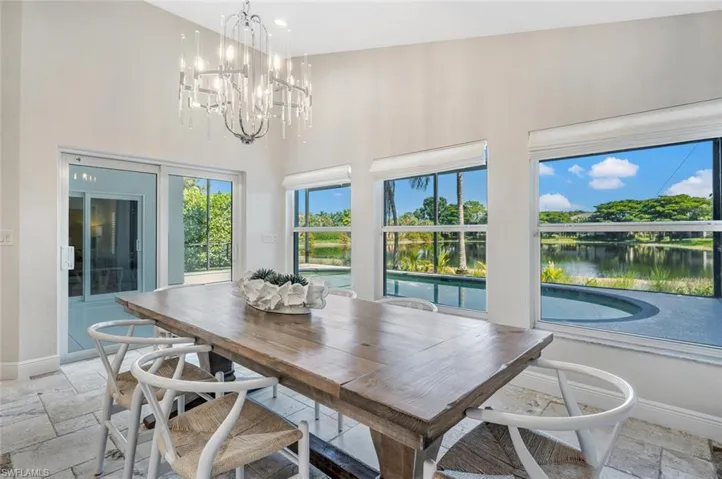 Dining space with a notable chandelier, a water view, light tile patterned floors, and high vaulted ceiling