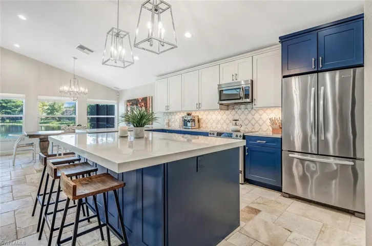 Kitchen featuring lofted ceiling, appliances with stainless steel finishes, pendant lighting, light tile patterned floors, and a kitchen island