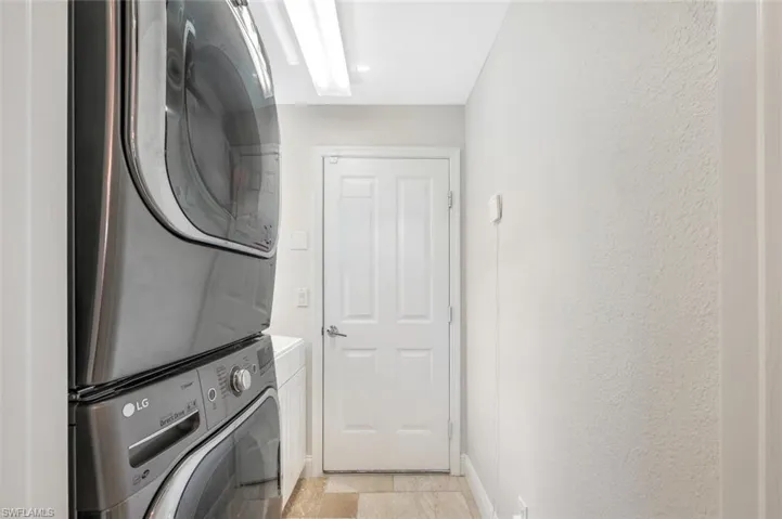 Clothes washing area featuring light tile patterned floors and stacked washer / drying machine